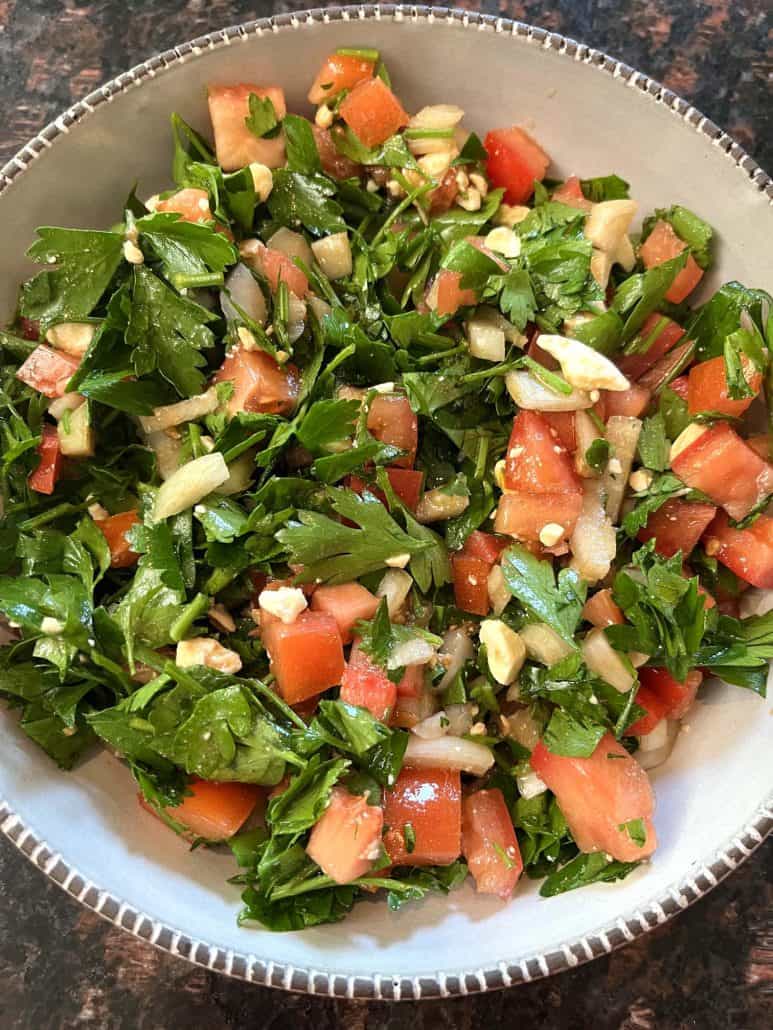 A bowl of healthy parsley-based salad, featuring chopped parsley, tomatoes, onions, and feta, mixed with a balsamic vinegar and olive oil dressing.