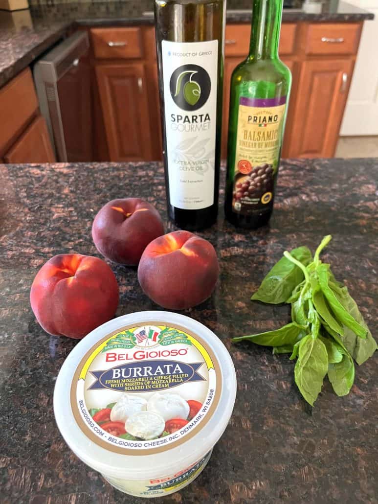 Ingredients for peach burrata salad, including fresh peaches, creamy burrata cheese, basil leaves, and a drizzle of balsamic vinegar and olive oil.