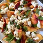 Top view of a peach burrata salad on a white plate.