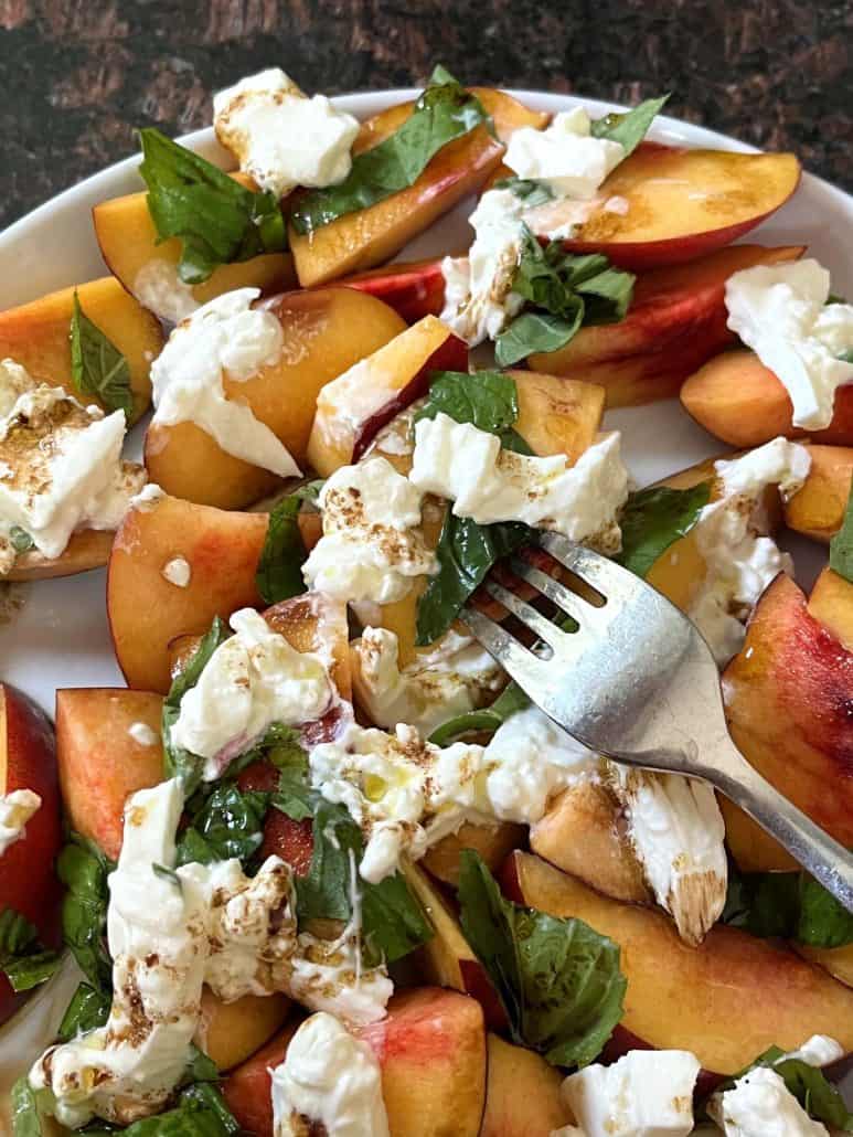 Peach burrata salad being lifted by a fork.