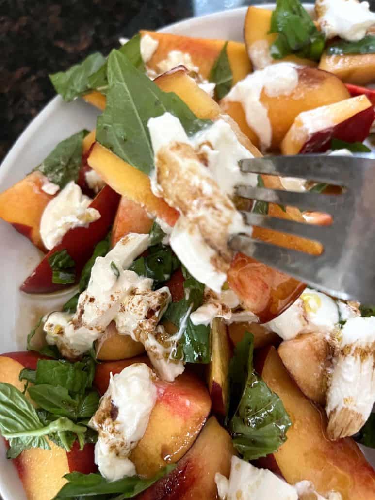 Close-up of a fork lifting a portion of peach burrata salad