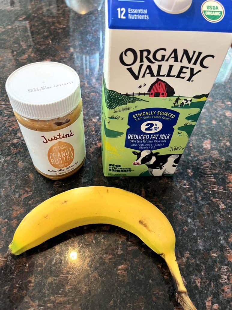 Simple ingredients for the Peanut Butter Banana Smoothie, including a ripe banana, a jar of Justin's peanut butter, and a carton of Organic Valley 2% reduced-fat milk.