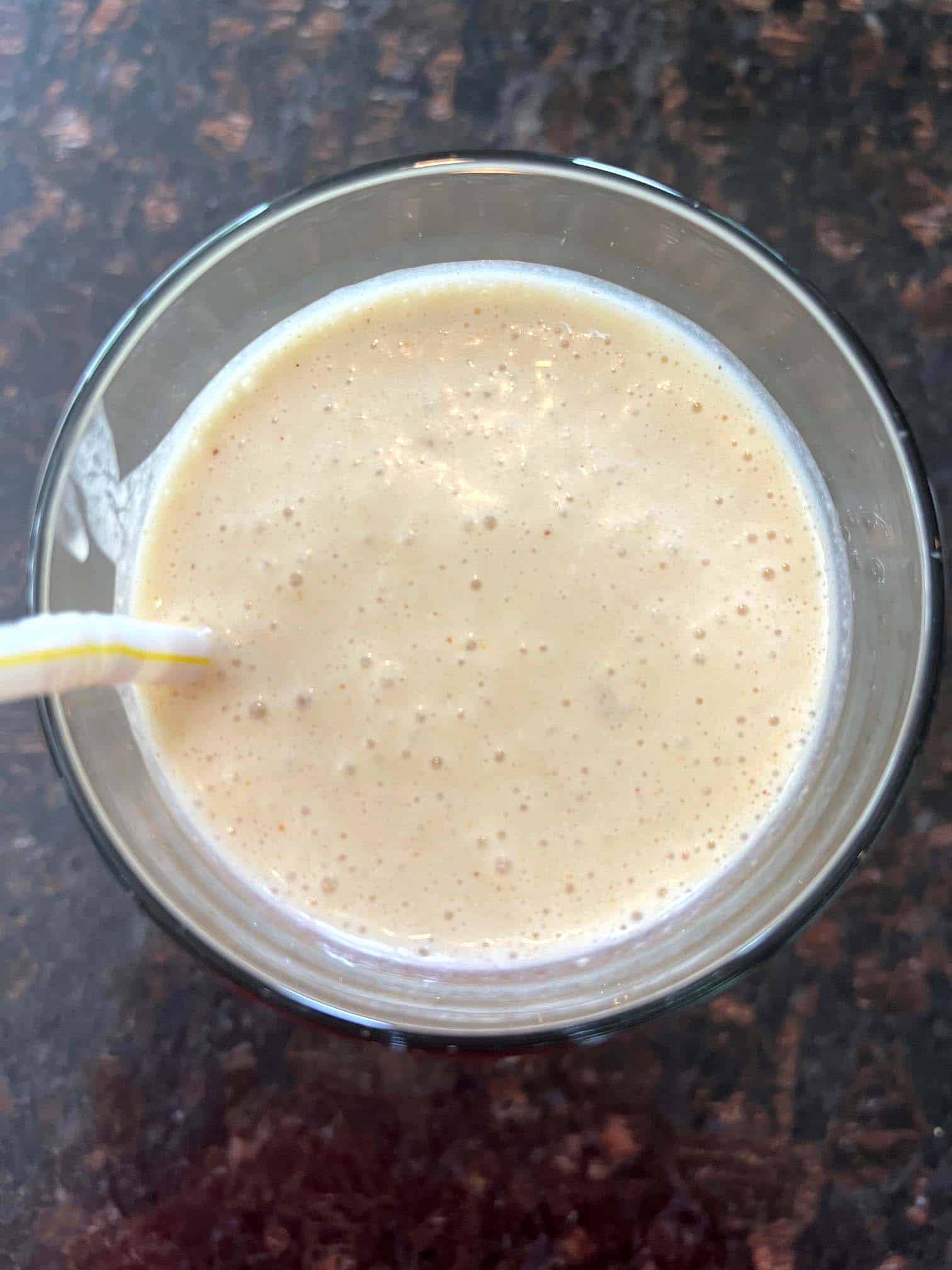 A top-down view of a creamy Peanut Butter Banana Smoothie in a glass with a yellow straw.