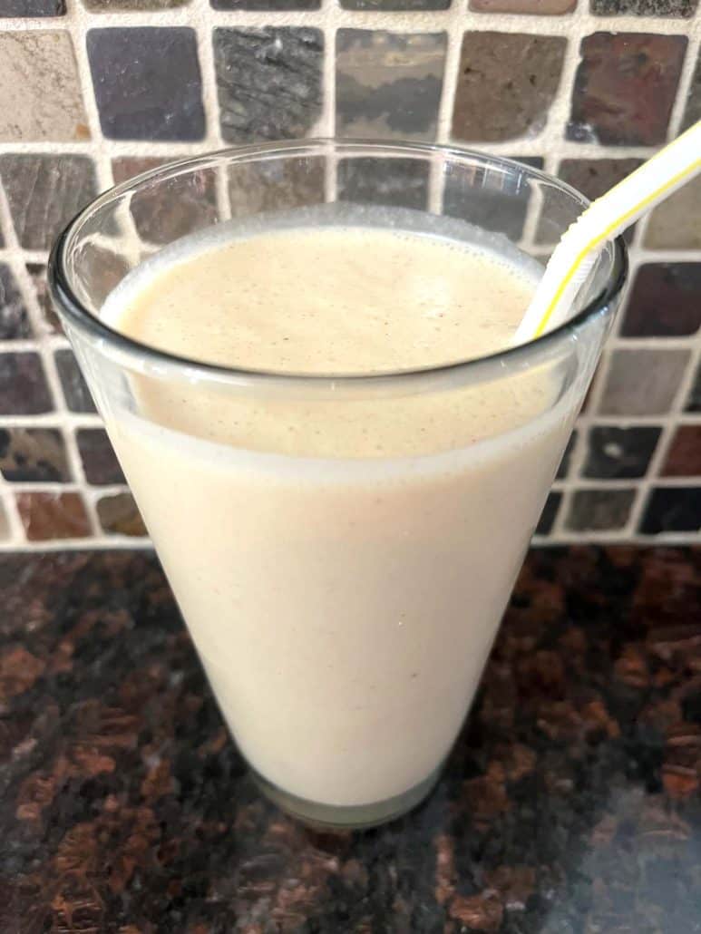 A tall glass filled with a freshly blended Peanut Butter Banana Smoothie, complete with a yellow straw. A perfect healthy and refreshing creamy smoothie for breakfast or a snack. 