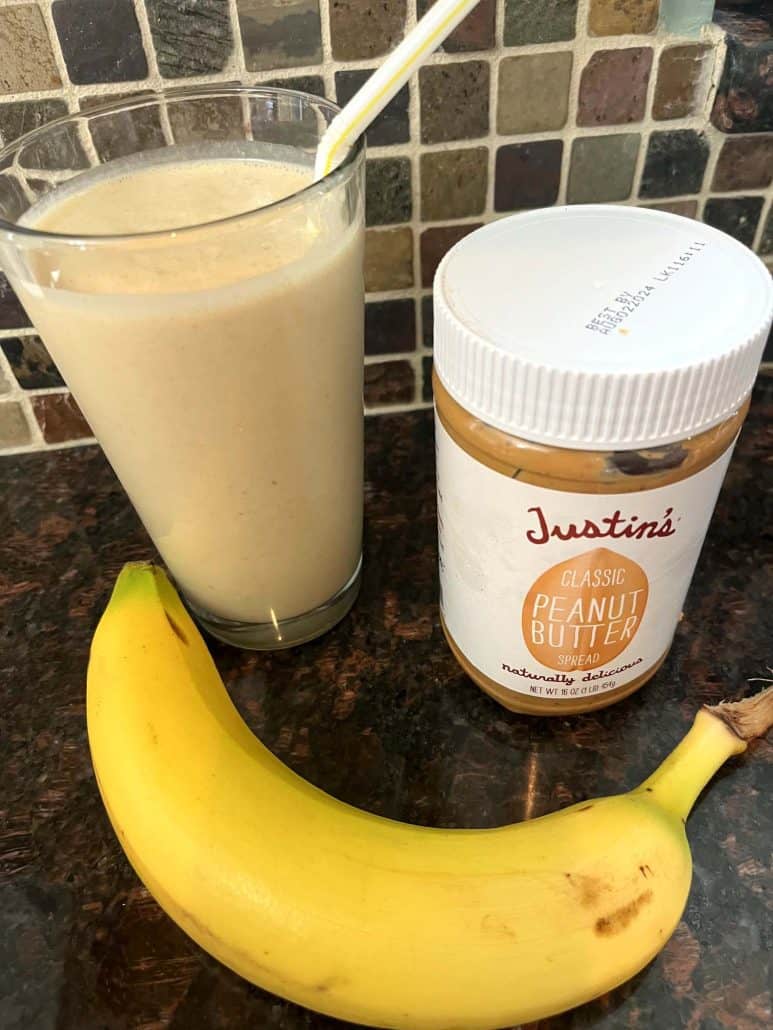 A freshly made Peanut Butter Banana Smoothie in a tall glass with a straw, placed next to it's simple ingredients.