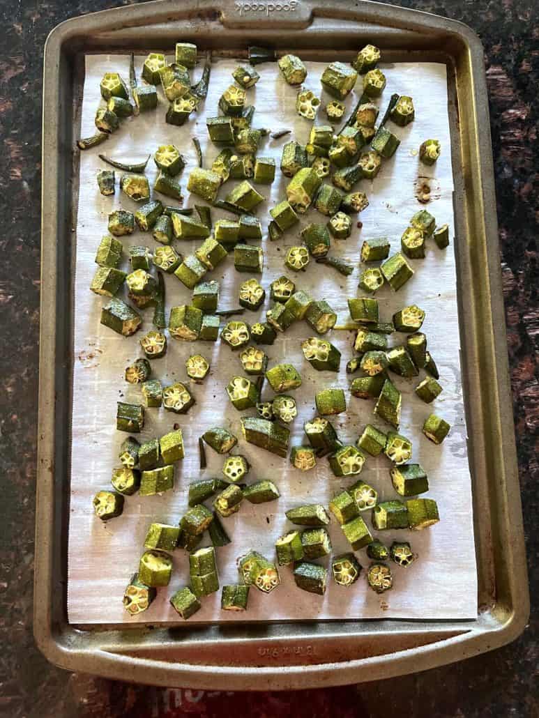 Top view of a baking sheet with roasted okra spread out on parchment paper.