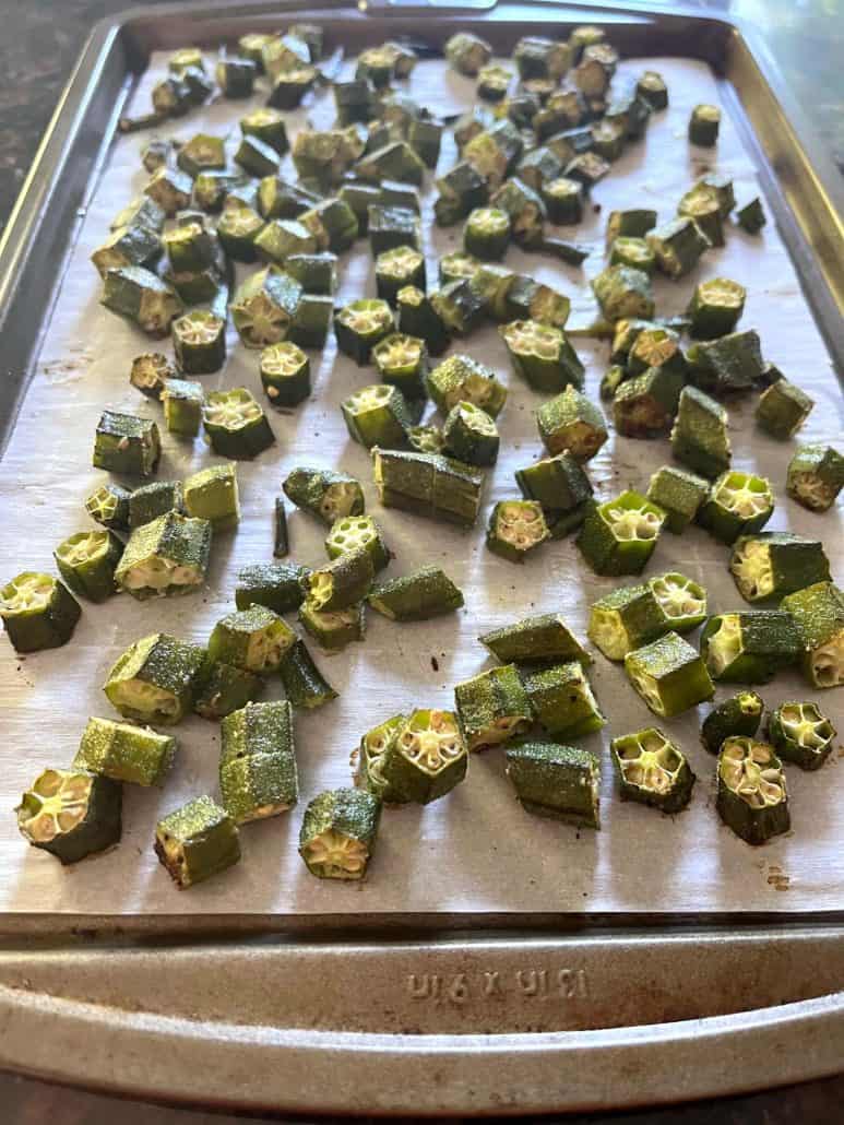 Baking sheet filled with evenly spaced roasted okra on parchment paper.