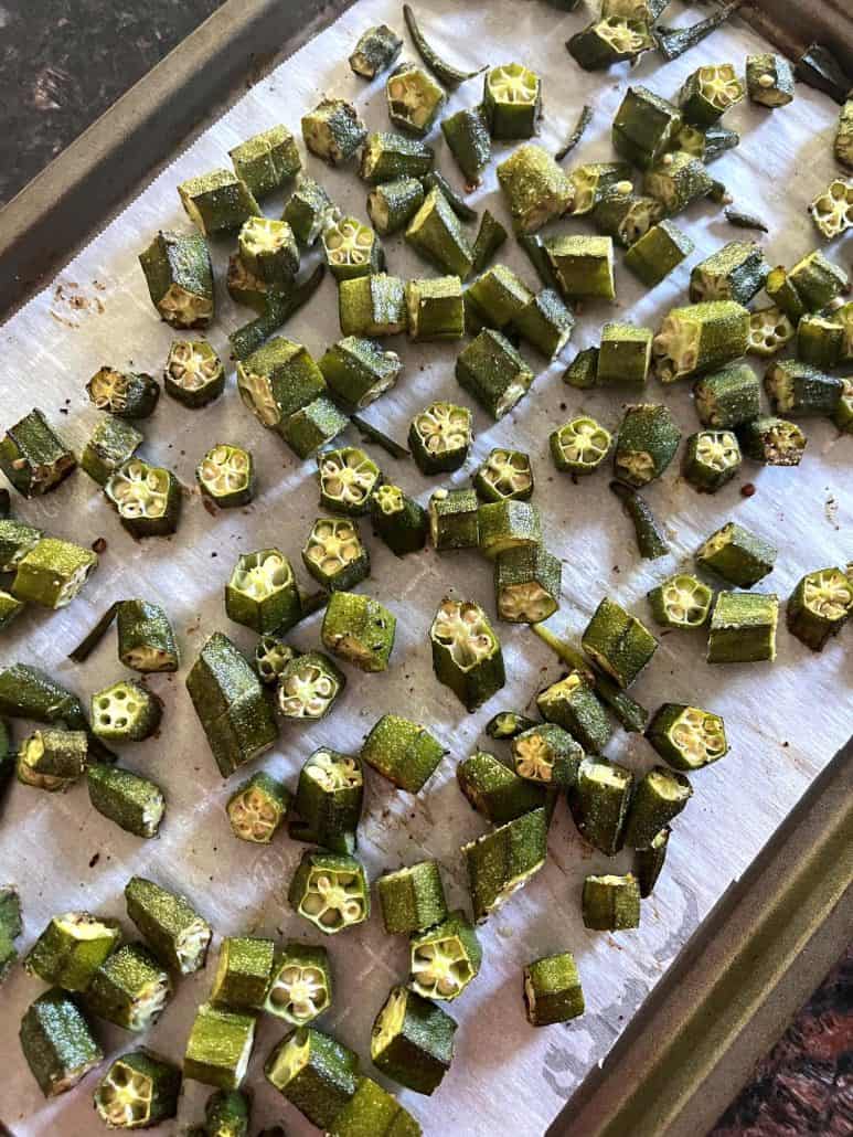 Roasted okra spread across a parchment-lined baking sheet.