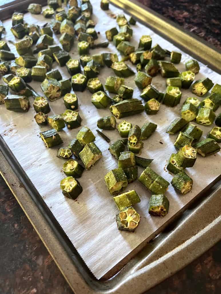 Parchment-lined baking sheet filled with evenly spaced roasted okra pieces.