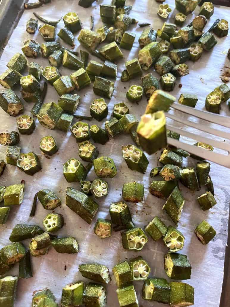 Roasted okra pieces on a parchment-lined baking sheet, with a fork holding two pieces.