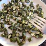 Crispy roasted okra slices served on a white plate while a fork is holding two pieces of okra.