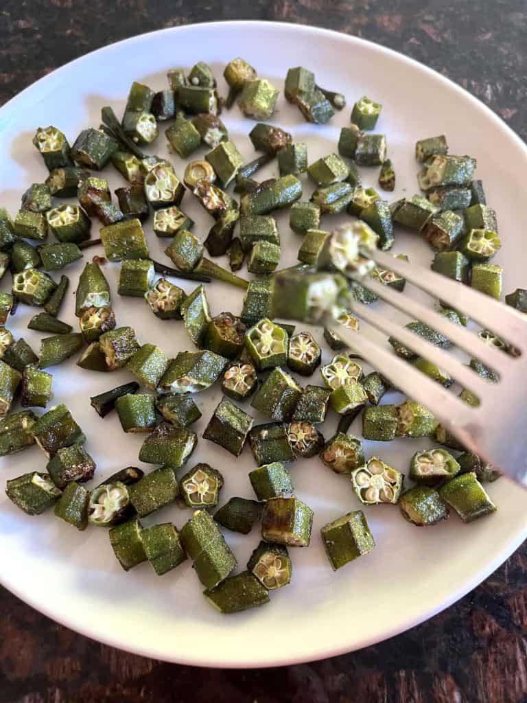 Crispy roasted okra slices served on a white plate while a fork is holding two pieces of okra.