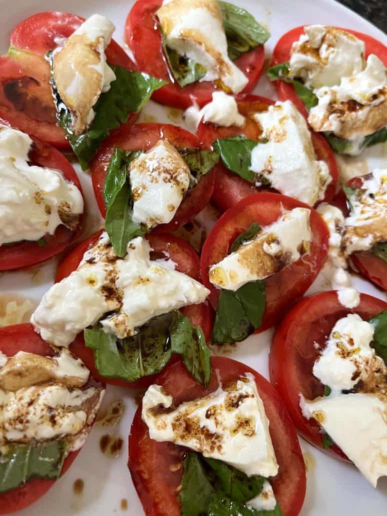 Close-up image of a fresh tomato burrata salad on a white plate. 