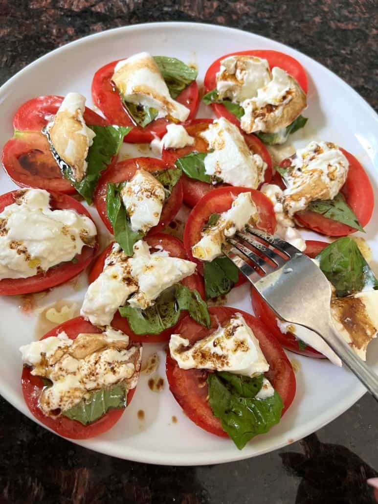 Top view of a tomato burrata salad served on a white plate.