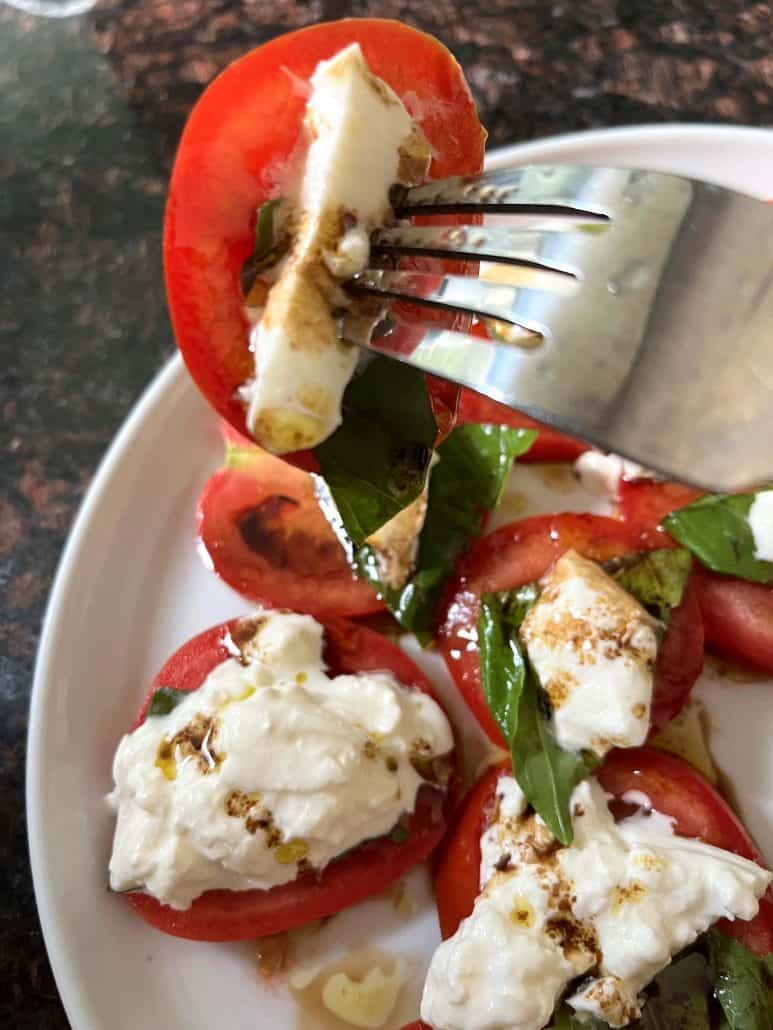 A fork holding a piece of tomato and burrata salad.