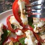 A fork carrying a portion of tomato and burrata salad.