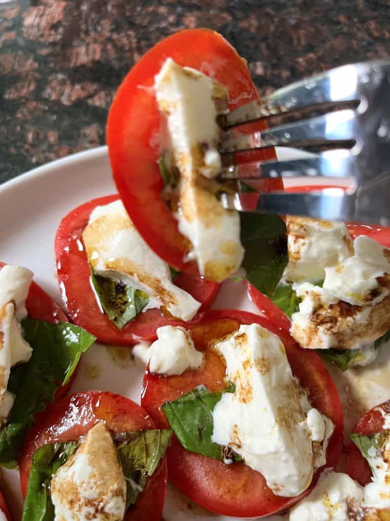 A fork carrying a portion of tomato and burrata salad.