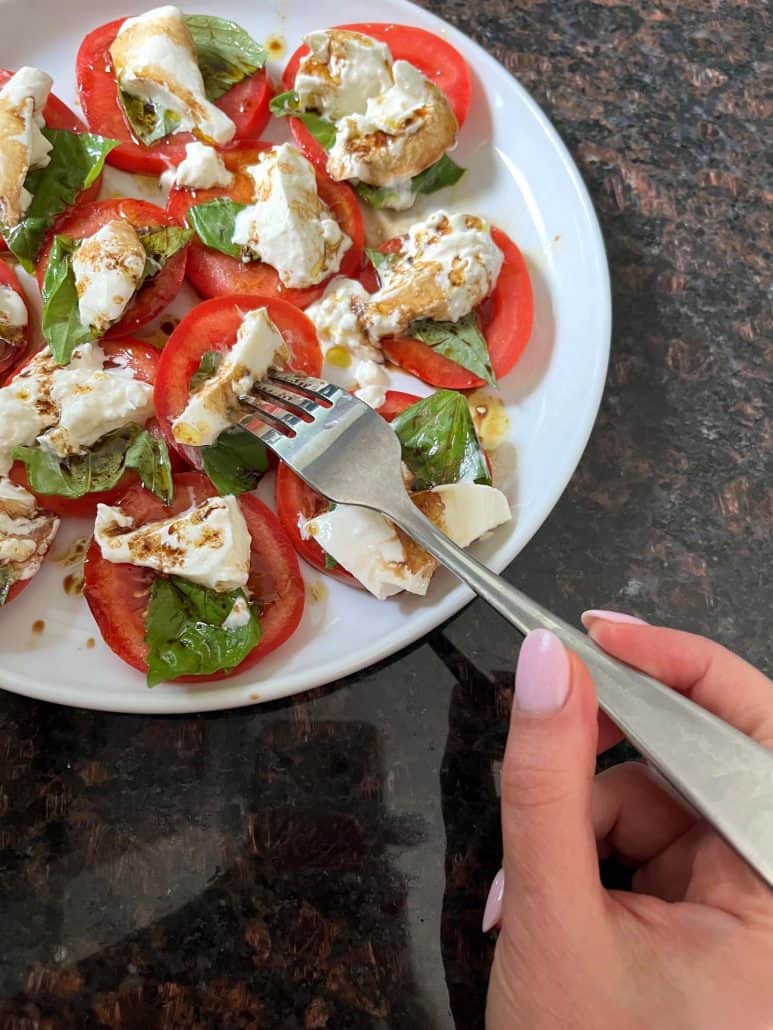 Melanie from melaniecooks.com piercing a tomato burrata salad with a fork.