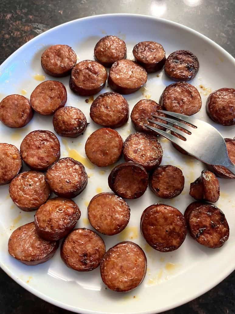 Andouille sausage slices on a white plate, with a fork ready for serving.