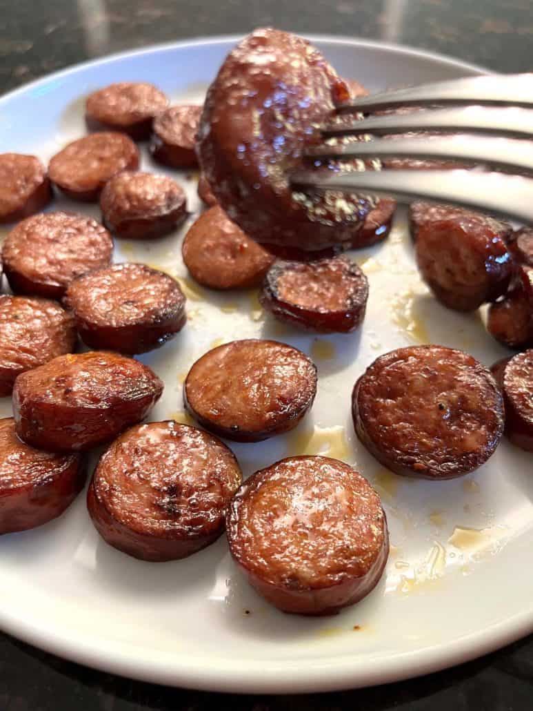 A fork holding a crispy slice of air-fried andouille sausage above a plate.