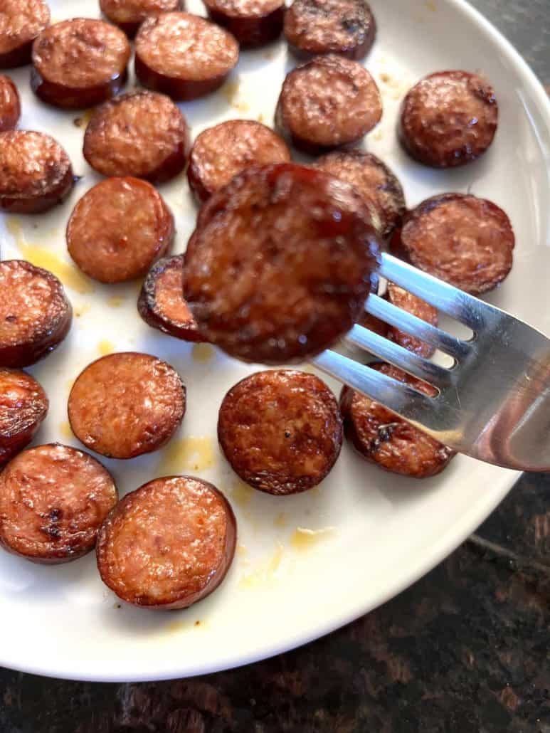 Crispy andouille sausage slice on a fork, with more slices on a plate in the background.