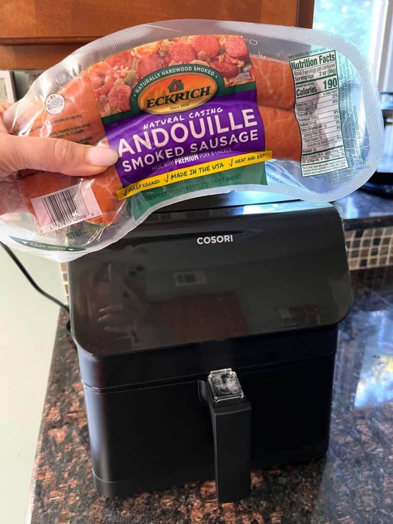 Packaged andouille smoked sausage held above an air fryer, ready to be cooked.