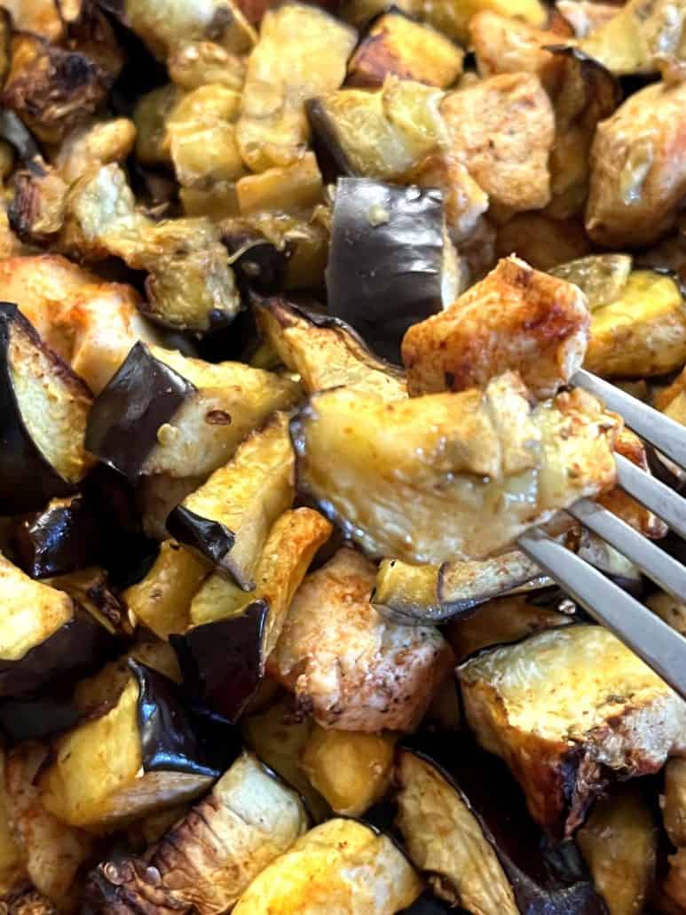 Close-up view of a fork holding a piece of juicy chicken with air-fried eggplant.