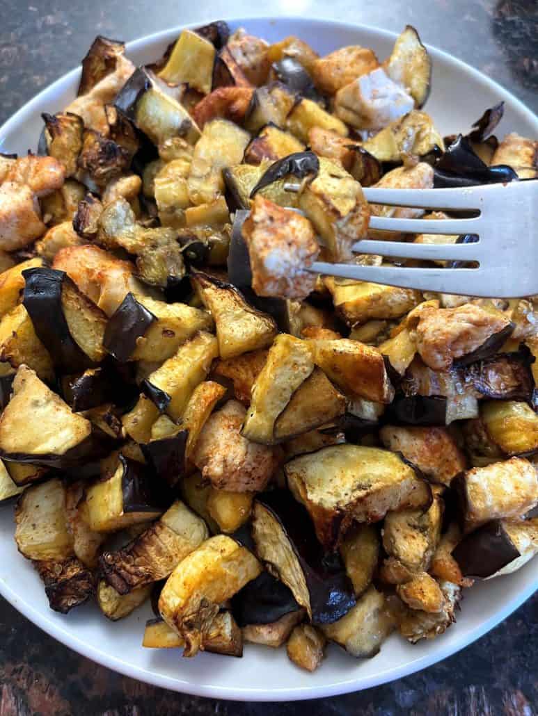 A plate of cooked chicken and eggplant with a fork holding a bite-sized piece, showing the final dish from the Air Fryer Chicken and Eggplant recipe.