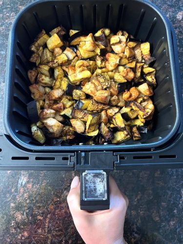 Hand holding the air fryer basket filled with golden-brown chicken and eggplant, showcasing the crispy result of the Air Fryer Chicken and Eggplant recipe.