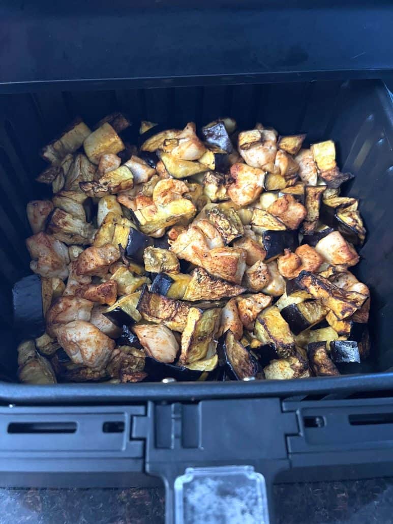 Cooked chicken and eggplant inside an air fryer basket.