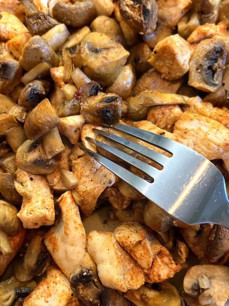 Fork digging into the seasoned and cooked chicken and mushrooms, showcasing the texture and tenderness.