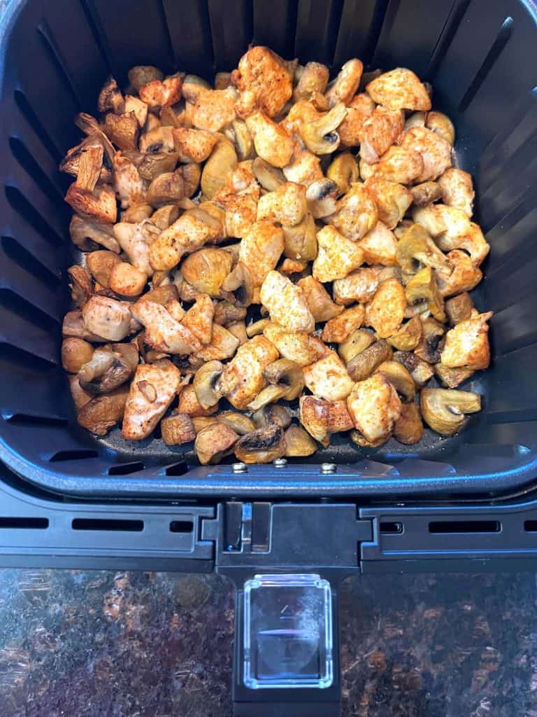 Air fryer basket filled with perfectly cooked, seasoned chicken and mushrooms.