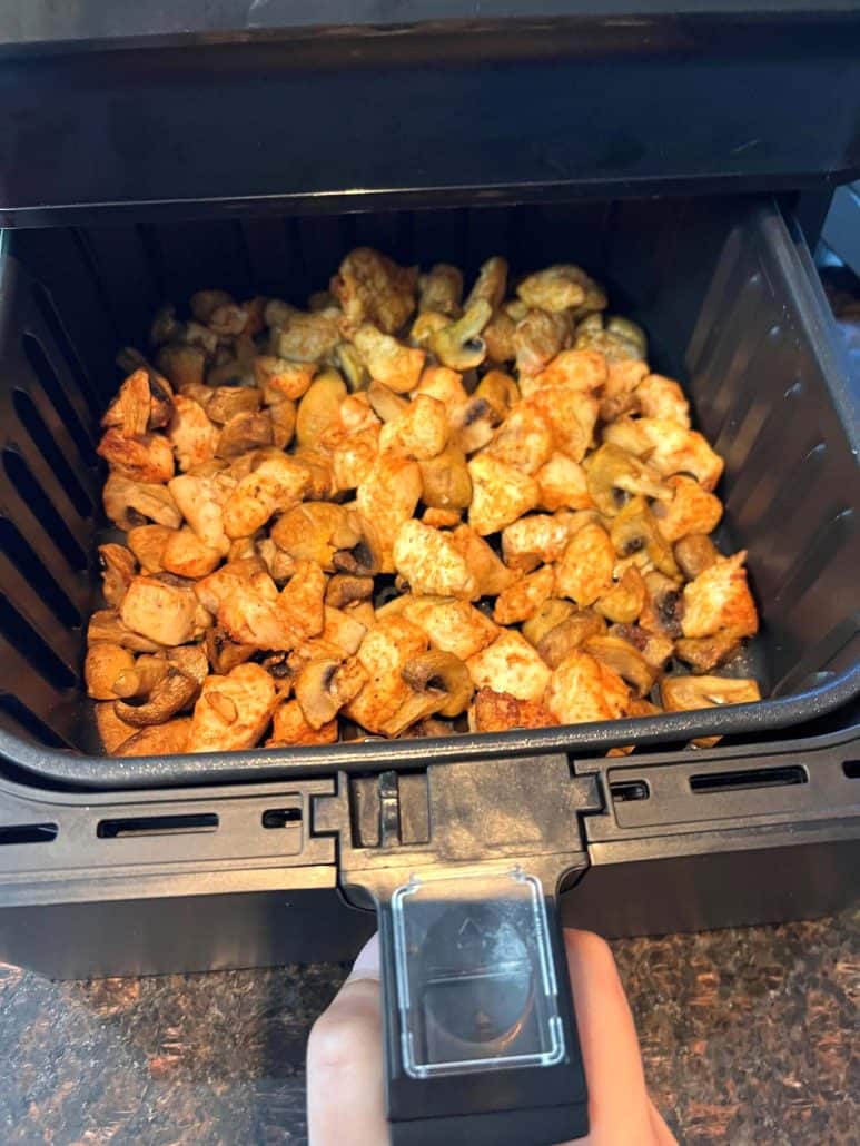 Freshly cooked chicken and mushrooms inside the air fryer, showing the perfectly browned and seasoned pieces.