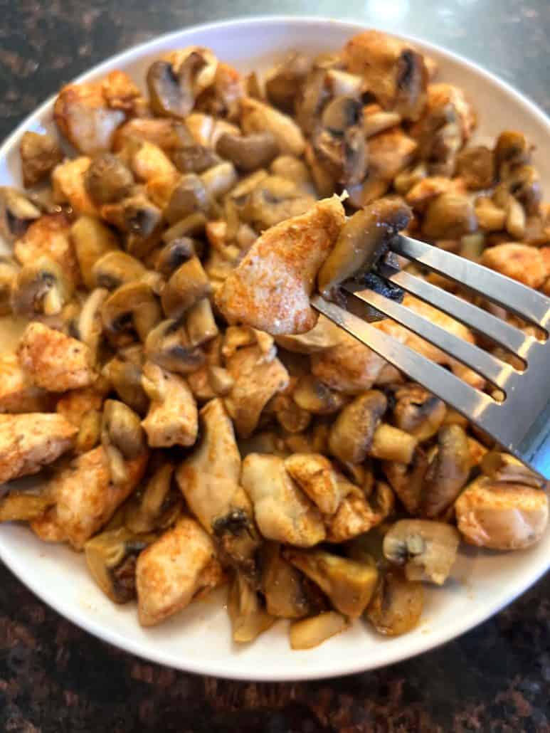 Fork holding a piece of juicy chicken and mushroom,highlighting the tender texture and flavors.