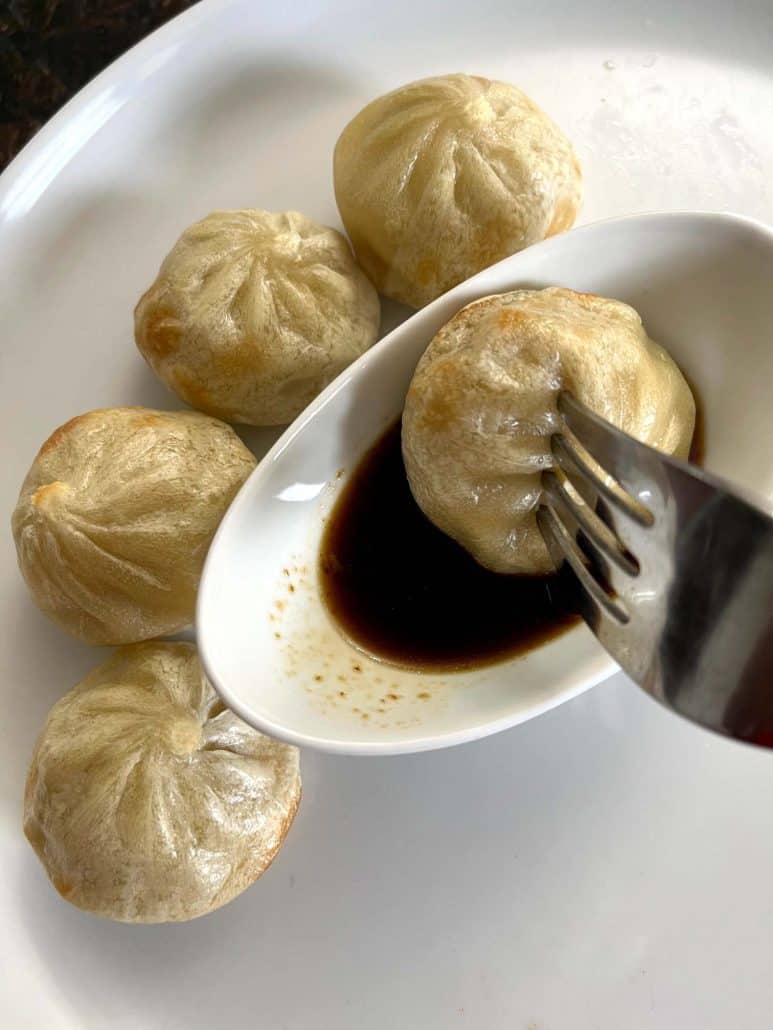 Fork dipping an air-fried Bibigo dumpling into soy sauce.