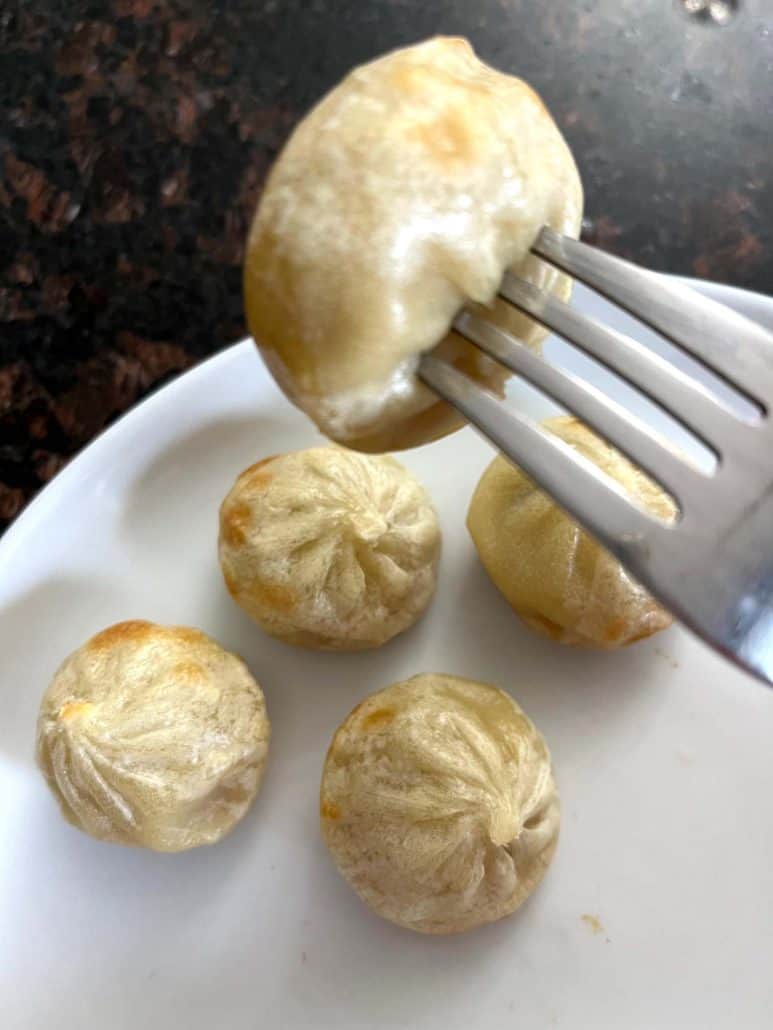 Fork holding an air-fried Bibigo dumpling above a plate, showing the golden, tender texture ready for dipping.