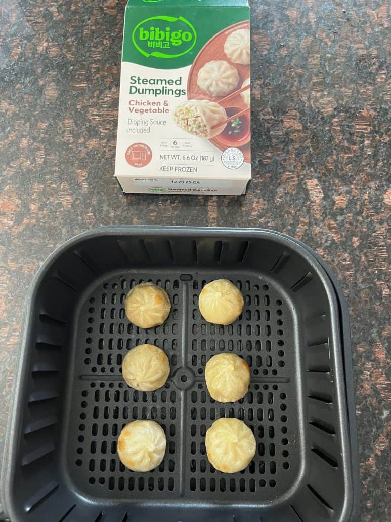 Air fryer basket with six golden-brown Bibigo dumplings next to the package.