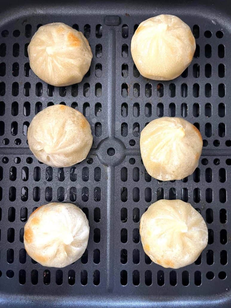 Close-up of six golden and slightly crisped Bibigo dumplings arranged in an air fryer basket.