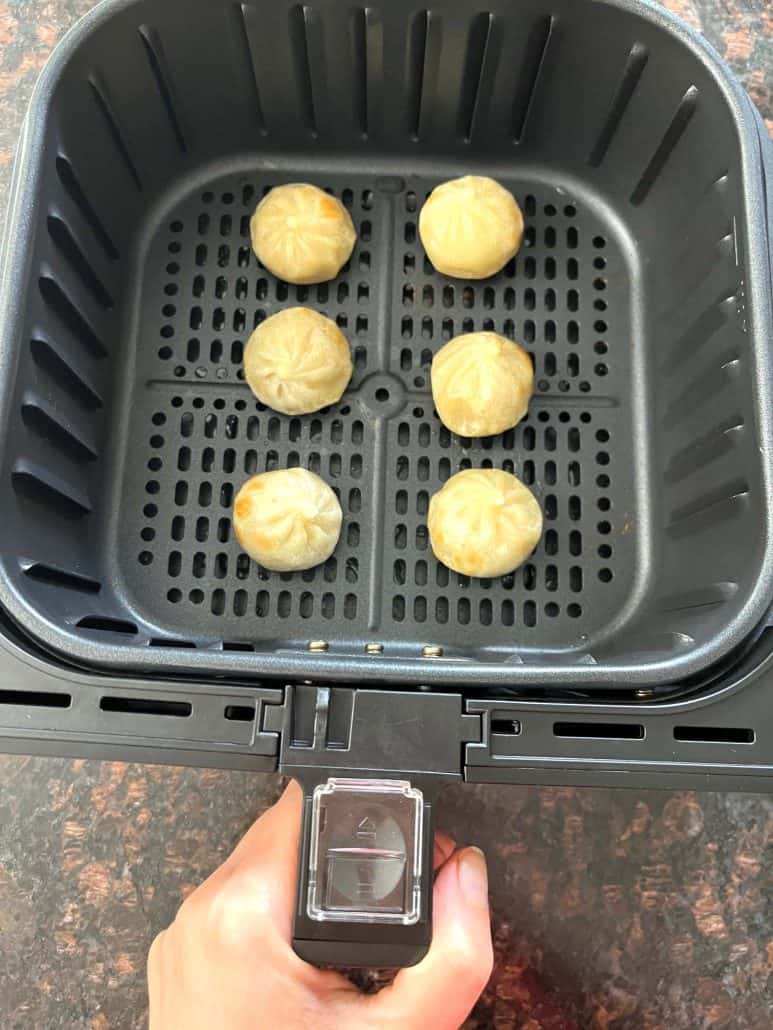 Hand of Melanie Mendelson from melaniecooks.com holding an air fryer basket with six cooked Bibigo dumplings.