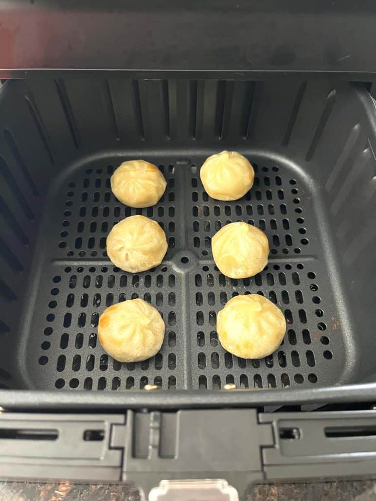 Six Bibigo dumplings cooked to golden perfection in an air fryer basket.