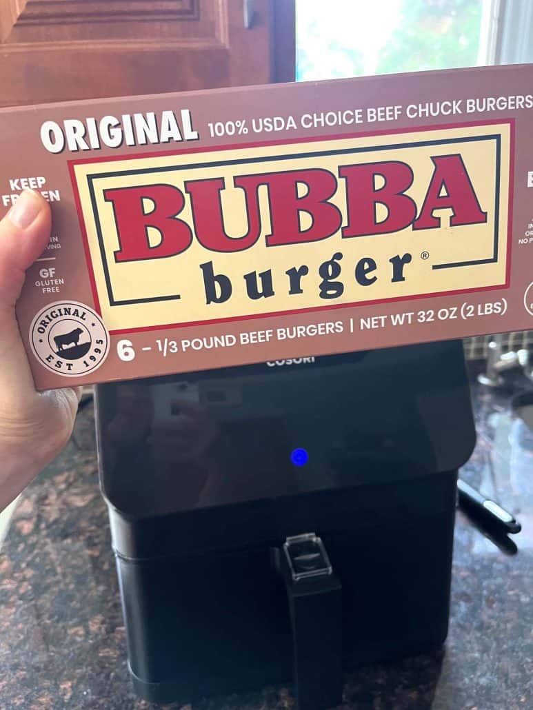 Hand holding a box of Original Bubba Burgers in front of an air fryer.