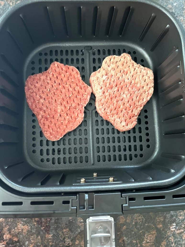 Two frozen Bubba Burger patties placed in an air fryer basket, ready to be cooked without defrosting.