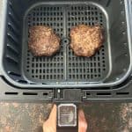 Two frozen Bubba Burgers cooking in an air fryer basket.