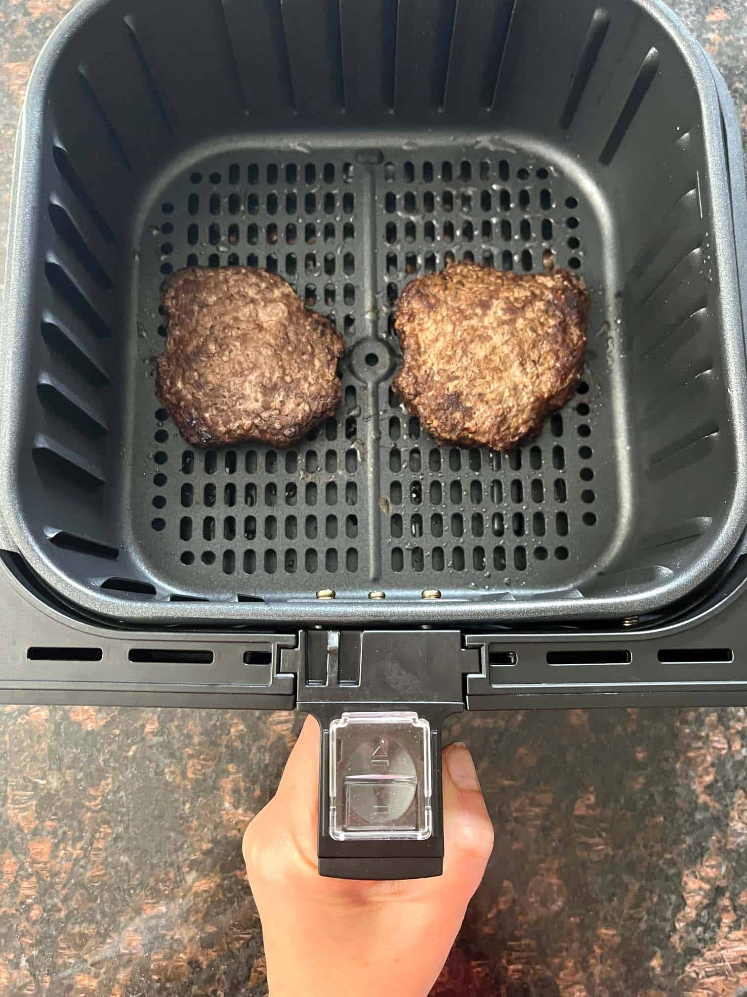 Two frozen Bubba Burgers cooking in an air fryer basket.