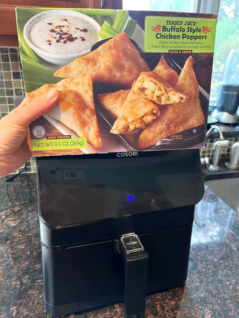 Holding a box of Trader Joe's Buffalo Style Chicken Poppers above an air fryer.