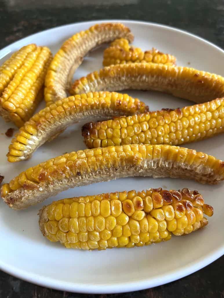 Close-up of crispy, air-fried seasoned corn ribs served on a white plate.