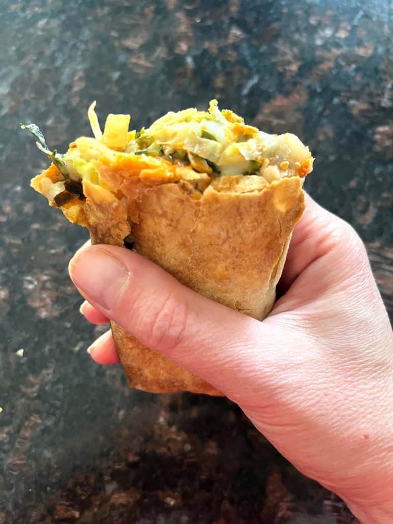 Holding a crispy Kati roll with a bite taken, revealing its spiced, and flavorful filling.