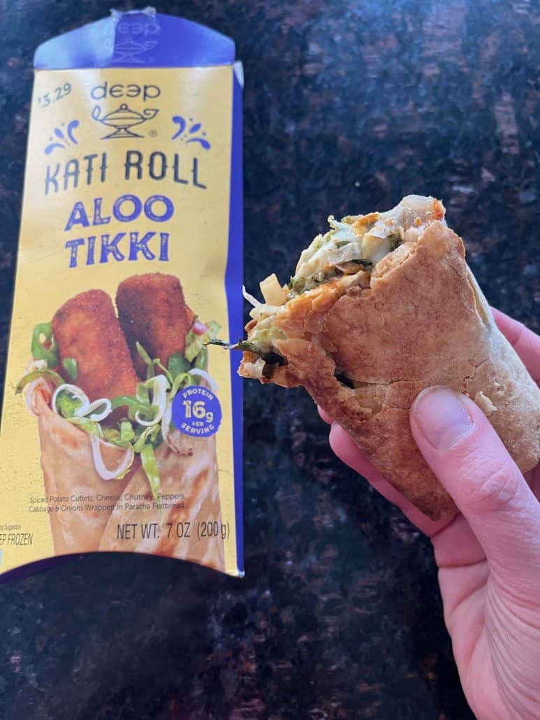 Holding a partially eaten Kati roll next to its packaging, showcasing the tasty Aloo Tikki filling.