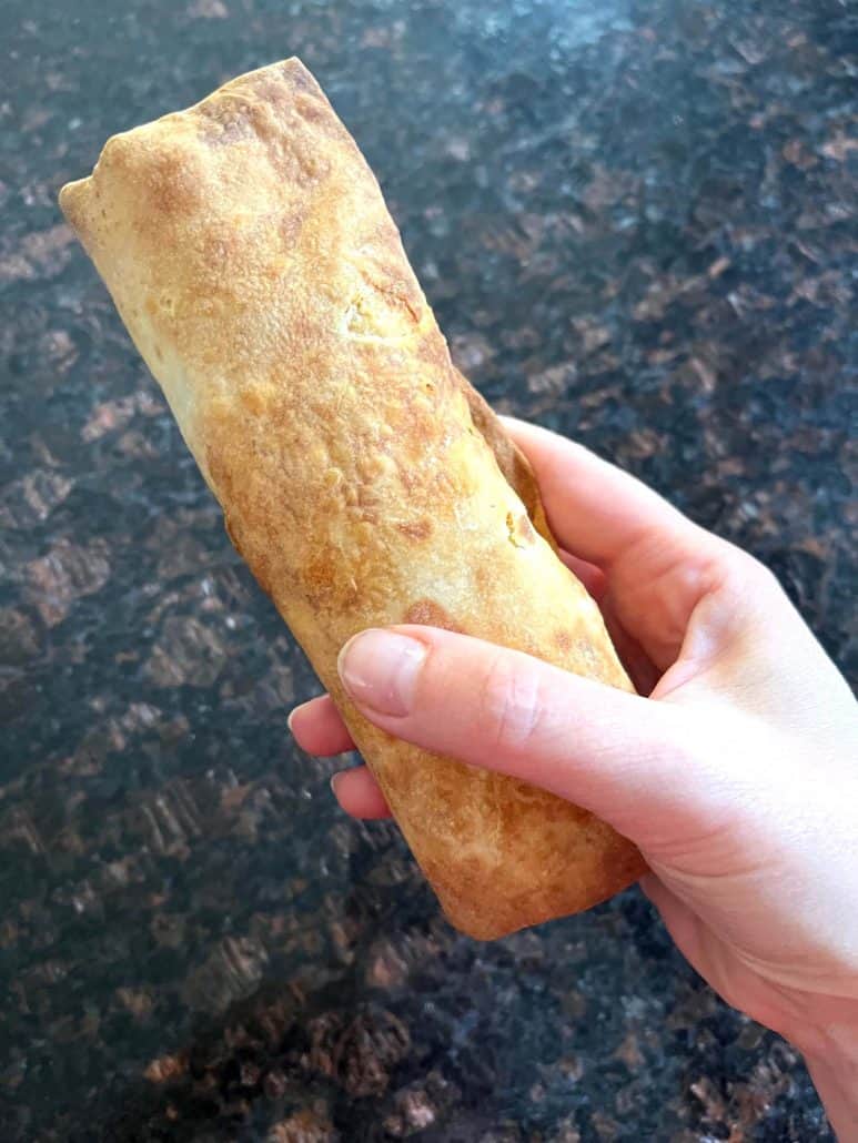 Holding a freshly air-fried Kati roll with a crispy, golden exterior, ready to enjoy as a quick and tasty snack.