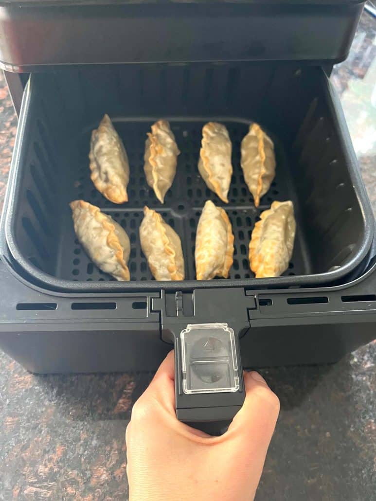 Pulling out an air fryer basket with perfectly cooked Mandu dumplings, ready to serve.